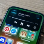 Ảnh iPhone 15 màu hồng hiển thị tính năng Dynamic Island với giao diện điều khiển nhạc trên màn hình khóa.