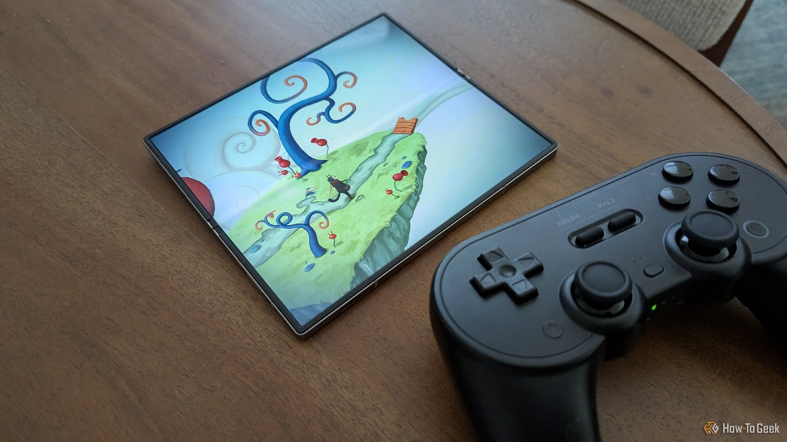 Chiếc điện thoại Samsung Galaxy Z Fold 6 đang hiển thị game Figment, đặt cạnh tay cầm chơi game 8BitDo Pro 2 màu xám, minh họa sự tương thích giữa điện thoại gập và phụ kiện chơi game chuyên nghiệp.