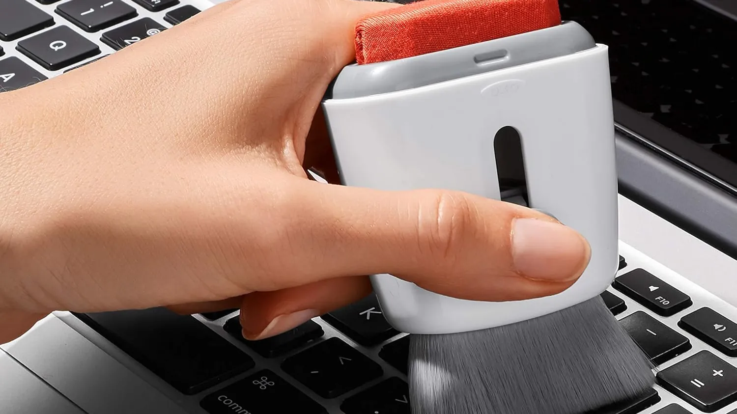 Chổi vệ sinh OXO Good Grips với hai đầu, một đầu cọ mềm và một đầu gạt silicone, dùng để làm sạch bàn phím.