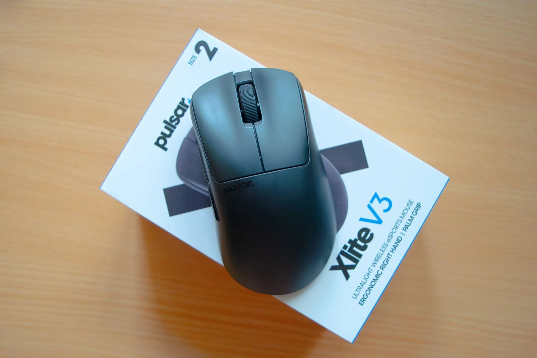 Chuột Pulsar Xlite V3 đặt trên hộp sản phẩm, thể hiện thiết kế tổng thể và màu sắc của chuột, đồng thời nhắc nhở về đặc điểm tiếng click to của nó có thể là một yếu tố cần cân nhắc khi sử dụng trong môi trường văn phòng chung.