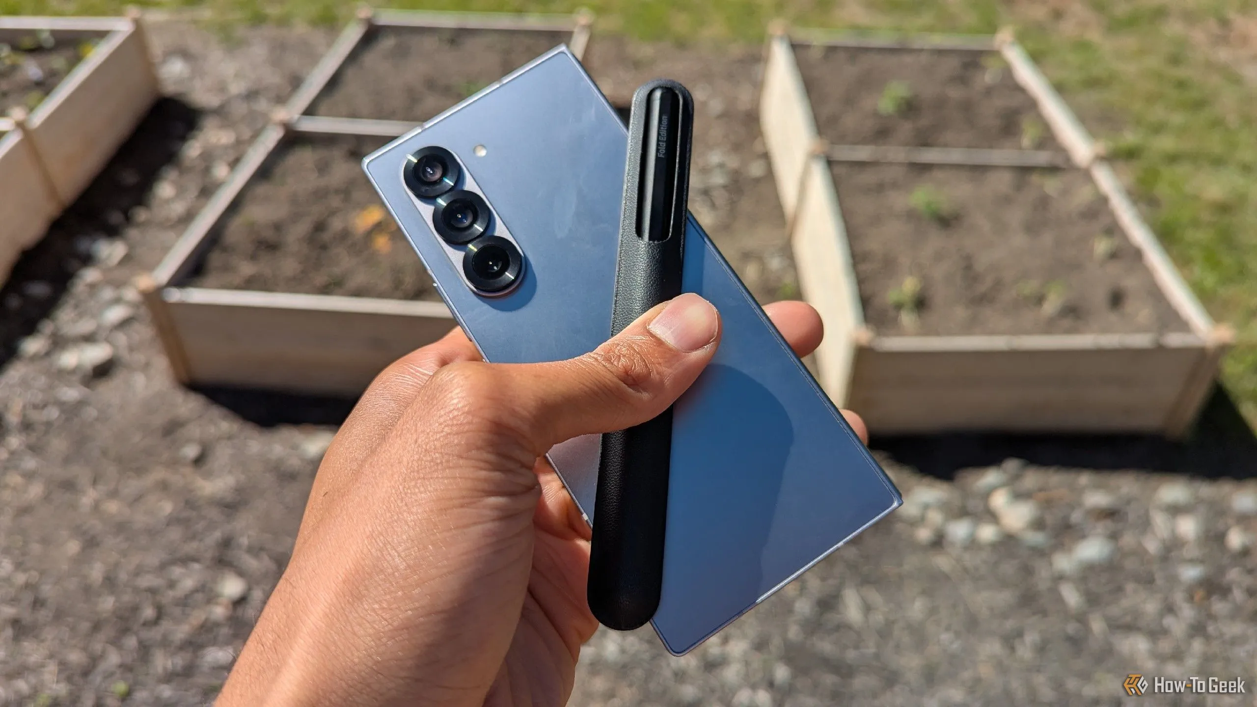 Điện thoại Samsung Galaxy Z Fold 6 cùng bút S Pen đặt trên mặt bàn gỗ với phông nền là khu vườn xanh mát, thể hiện khả năng làm việc linh hoạt và năng suất cao ở mọi nơi.