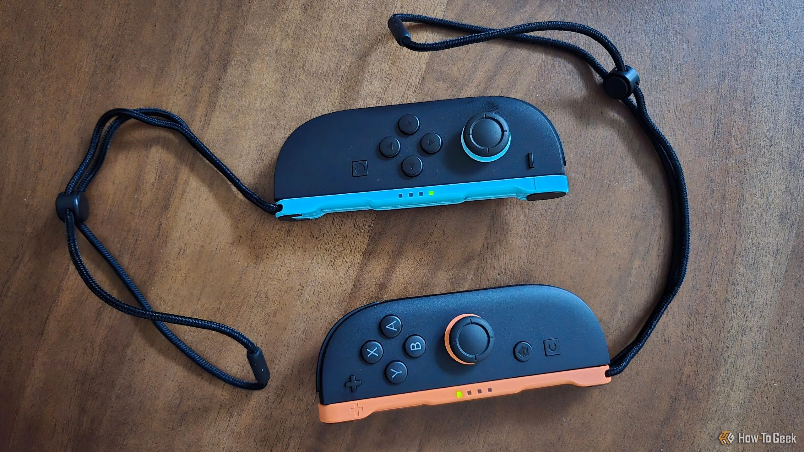 Đôi tay cầm Joy-Con 2 màu đỏ và xanh đặt trên bàn, đi kèm dây đeo cổ tay, sẵn sàng cho trải nghiệm chơi game.