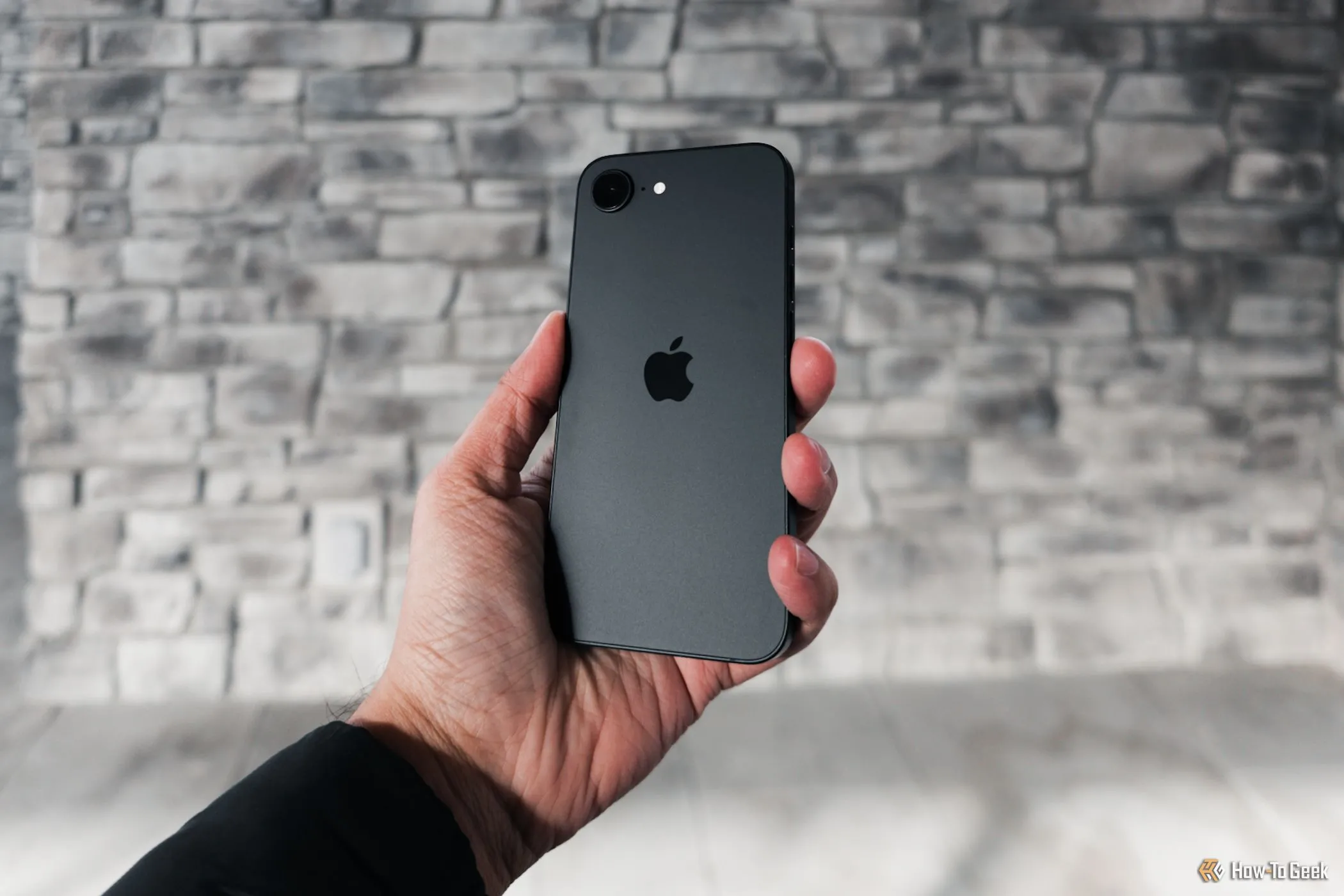 Góc nhìn nghiêng của iPhone 16e màu đen khi cầm trên tay, cho thấy cụm camera đơn gọn gàng và mặt lưng nhám tinh tế.