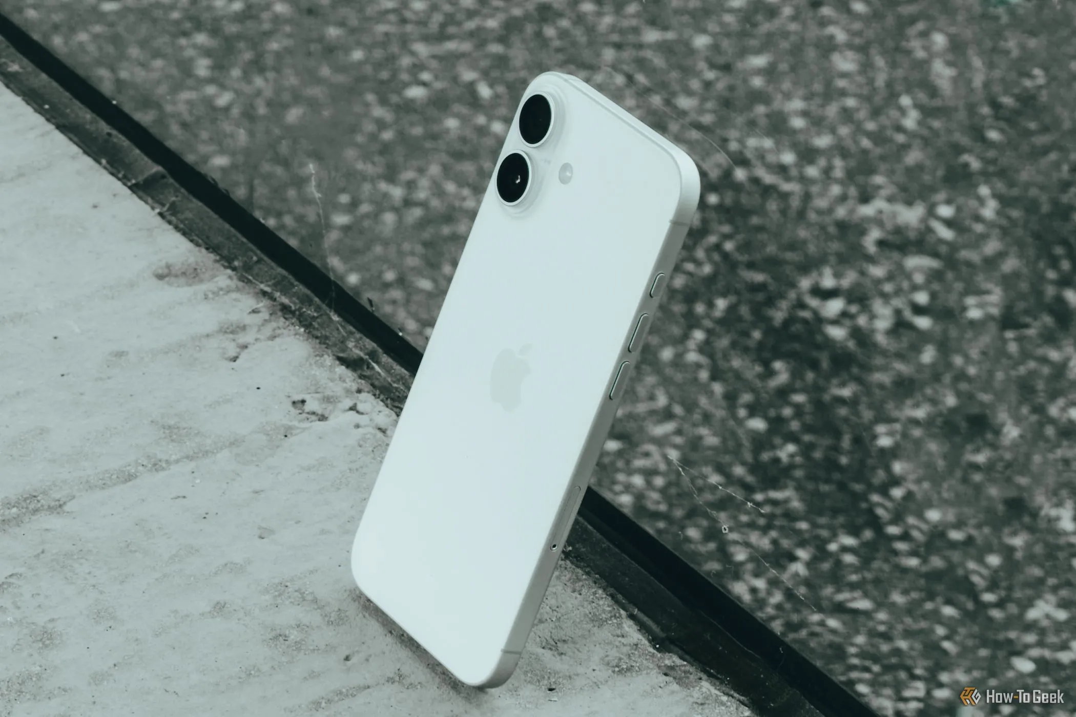iPhone 16 Plus đặt nghiêng dựa vào mặt kính, nhấn mạnh sự khác biệt về cụm camera kép so với camera đơn của iPhone 16e.