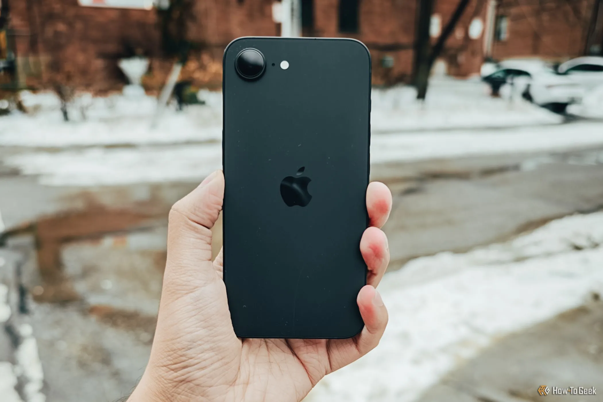 iPhone 16e màu trắng được cầm trên tay ngoài trời, làm nổi bật thiết kế cạnh phẳng và sự thoải mái khi cầm nắm.