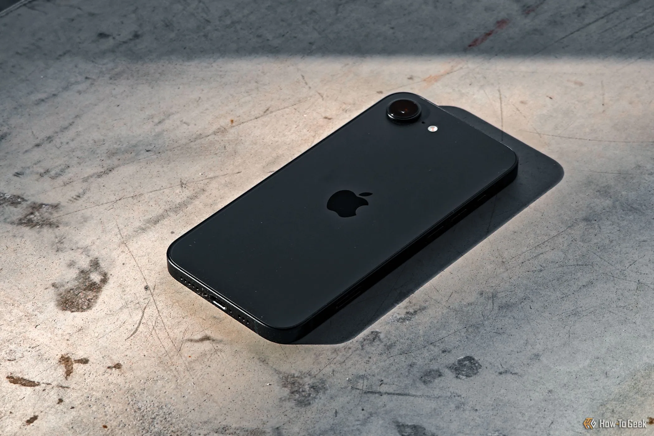 iPhone 16e úp mặt xuống nền bê tông, ám chỉ sự ổn định của kết nối di động nhờ modem C1 mới của Apple.