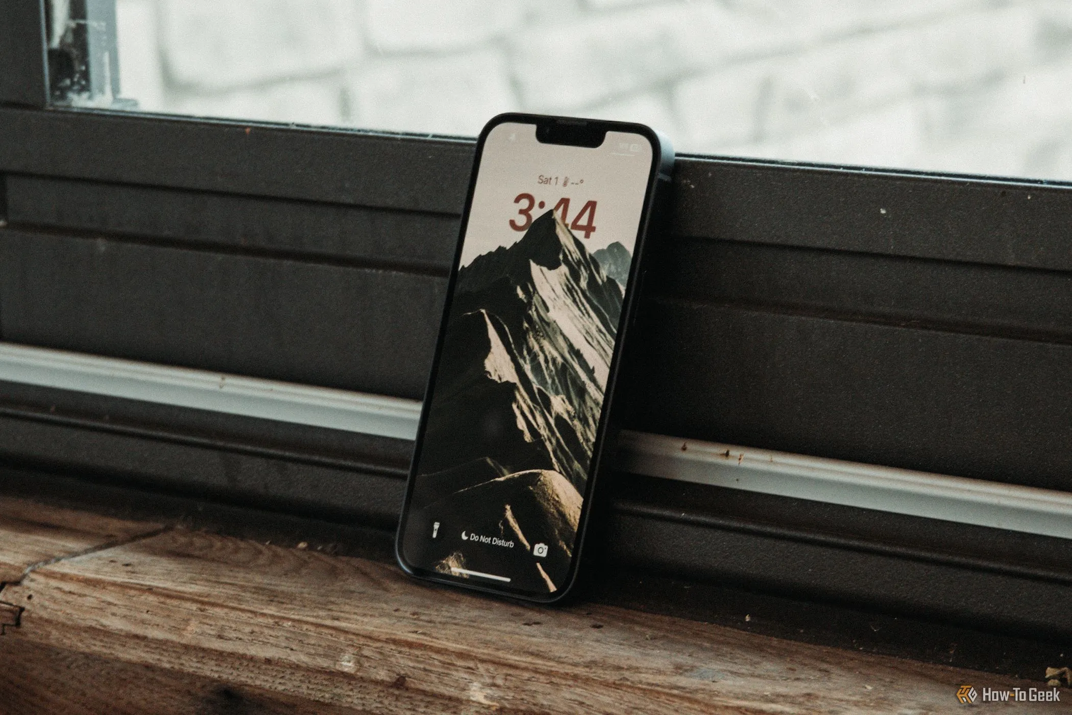 Màn hình khóa iPhone 16e hiển thị tai thỏ truyền thống, đặt nghiêng trên bệ cửa sổ, nhấn mạnh sự vắng mặt của Dynamic Island.