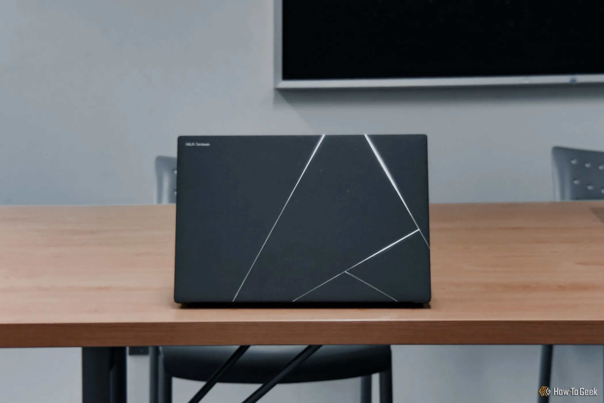 Mặt lưng ASUS Zenbook S 14 (2024) màu xám Zumaia đặt trên bàn gỗ, thể hiện vẻ ngoài sang trọng và tinh tế của dòng laptop cao cấp này.