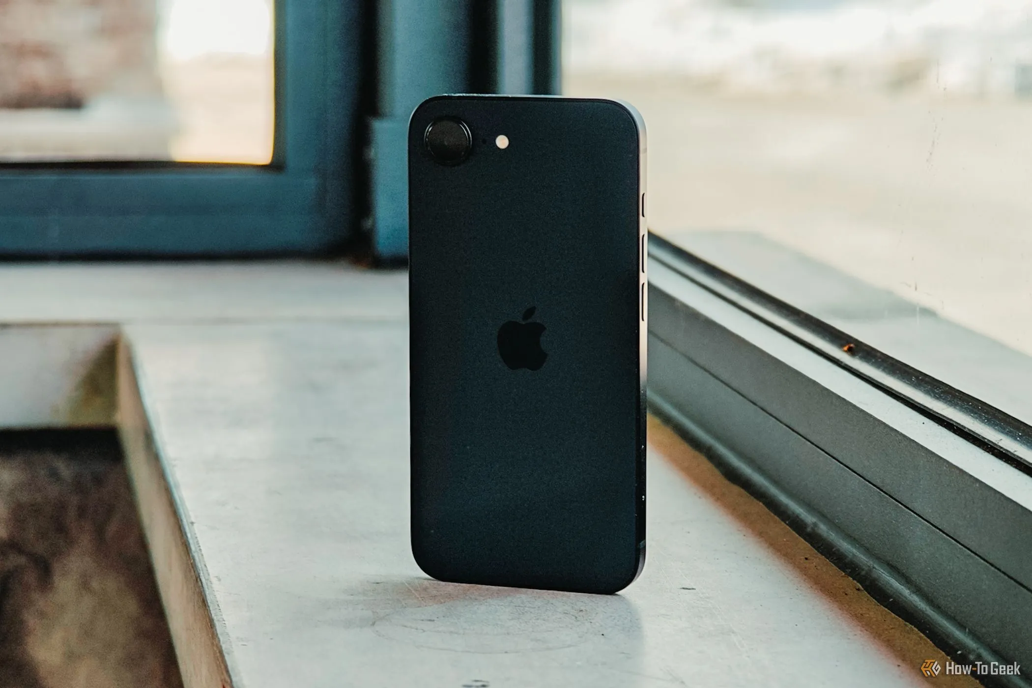 Mặt lưng iPhone 16e màu trắng nhìn từ góc nghiêng trước cửa sổ, tượng trưng cho hiệu năng mạnh mẽ của chip A18 và thời lượng pin vượt trội.