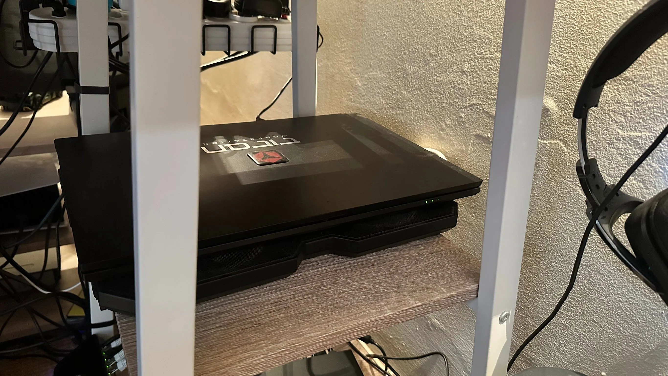 Một chiếc laptop đang đóng, đặt gọn gàng trên giá đỡ làm mát trên kệ bàn, tối ưu không gian làm việc.