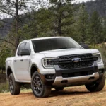 Một chiếc xe bán tải Ford Ranger XLT Sport màu trắng đời 2024 đang đỗ trên bãi cỏ, phía sau là cây cối xanh tươi, thể hiện thiết kế mạnh mẽ và linh hoạt của dòng xe này.