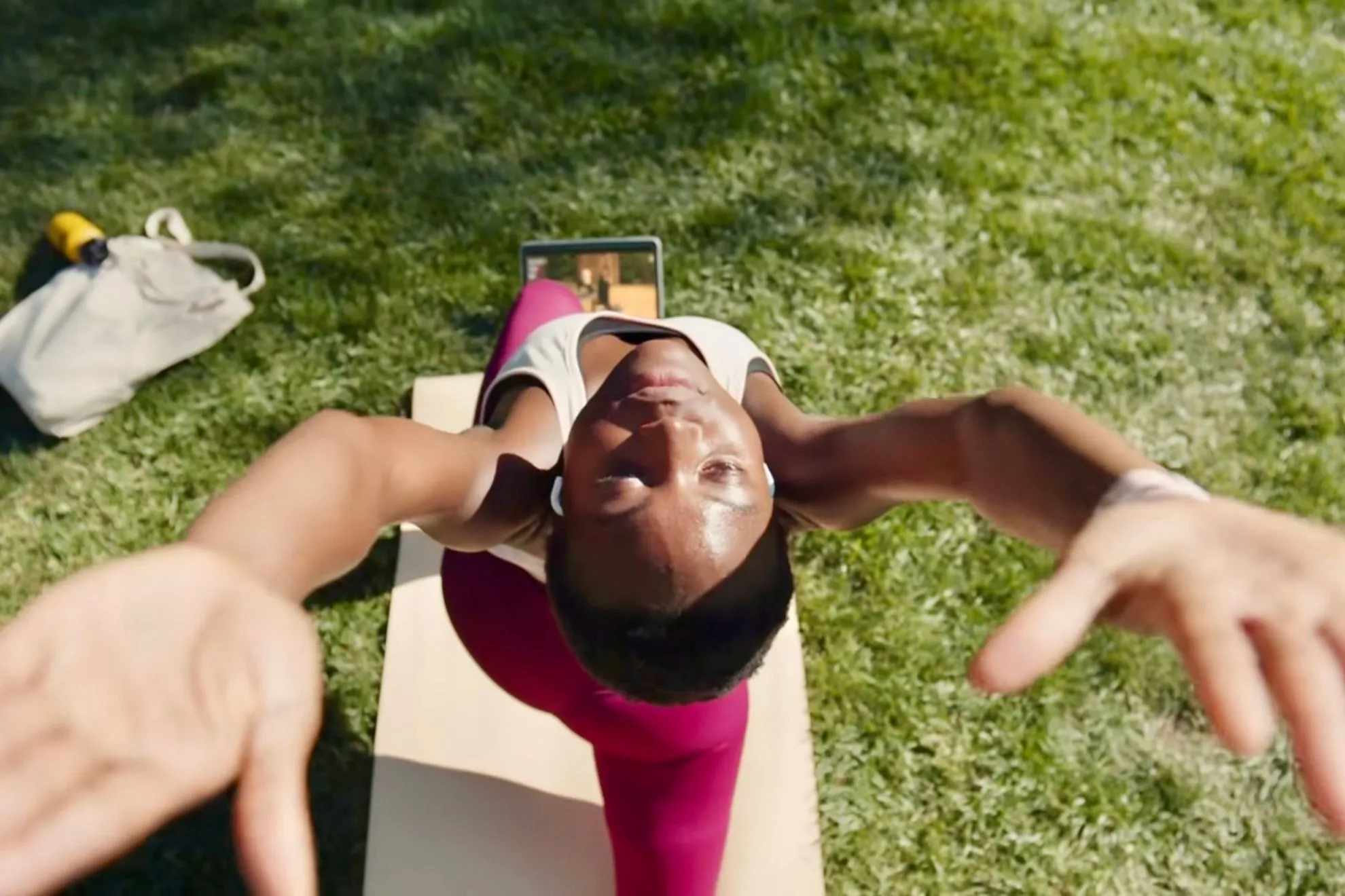 Người dùng thực hiện bài tập yoga với Apple Fitness+ trên iPad tại công viên, nhấn mạnh khả năng linh hoạt tập luyện ngoài trời và gần gũi với thiên nhiên.