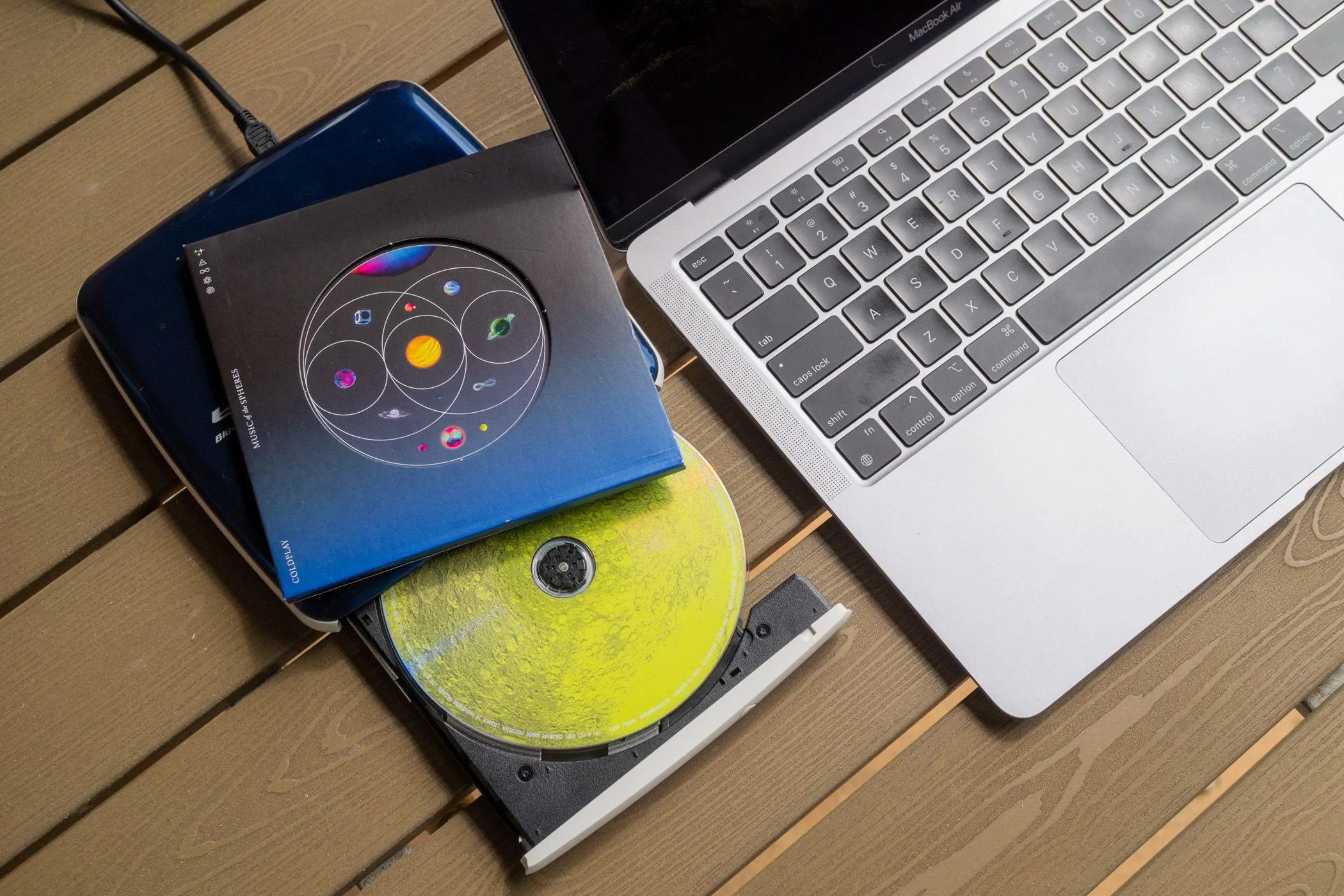 Ổ đĩa CD gắn ngoài và một đĩa nhạc được đặt cạnh MacBook Air, biểu thị cách kết nối để nhập nhạc số từ đĩa vật lý.
