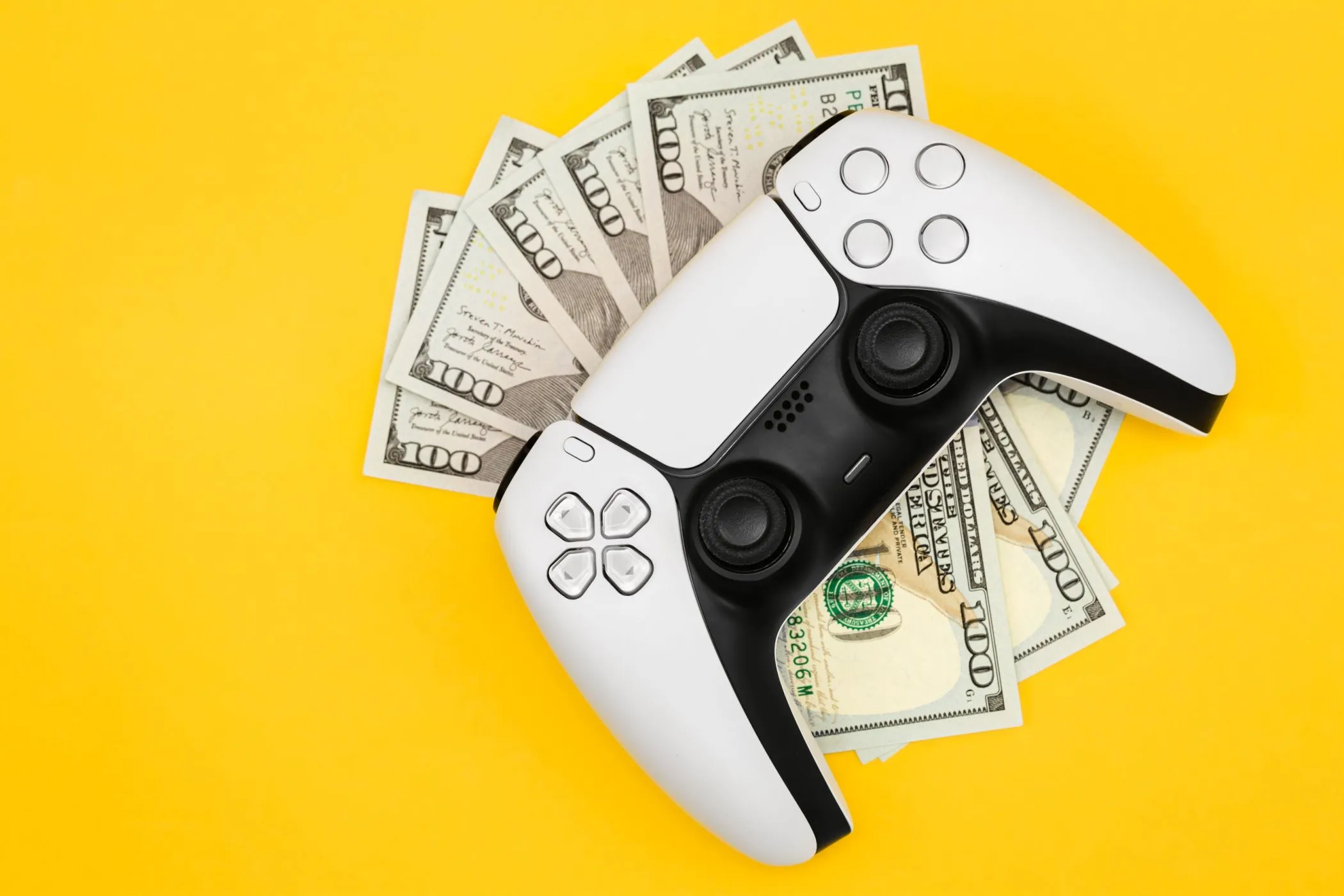 Tay cầm PlayStation 5 đặt trên năm tờ 100 đô la, tượng trưng chi phí phát triển game AAA tăng cao và giá game ngày càng đắt đỏ.